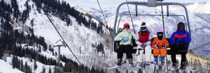 Four people sitting on a chair lift getting ready to ski down the mountain